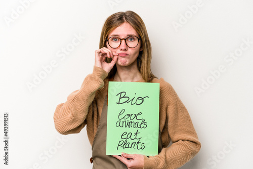 Young gardener woman holding a bio placard isolated on white background with fingers on lips keeping a secret. photo
