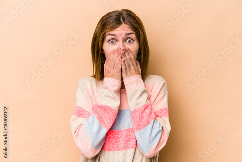 Young English woman isolated on beige background covering mouth with hands looking worried.