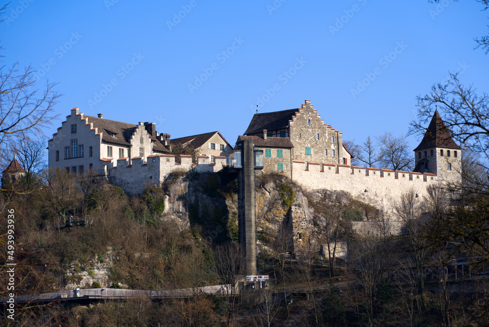 Famous Rhine Falls with rocks, splashing water and Laufen Castle on top of a hill on a sunny spring day, focus on background. Photo taken March 7th, 2022, Zurich, Switzerland.