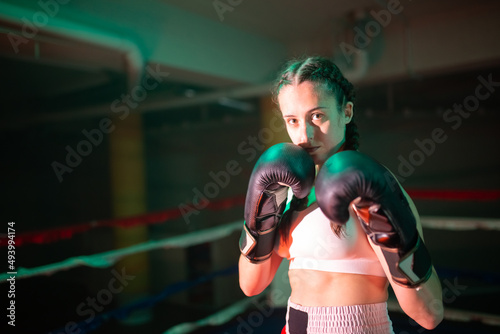 Portrait of serious girl standing in boxers pose. Beautiful Caucasian girl preparing for bout holding her hands in gloves defending face looking at camera. Female boxing and healthy lifestyle concept