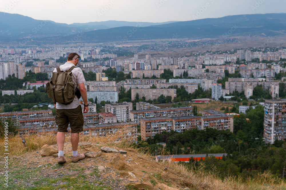A tourist with backpack poses against the backdrop of a densely populated area. Wretched high-rise buildings, dark gloomy tones. Copy space. Tbilisi Georgia. Zghvisubani III Micro-District