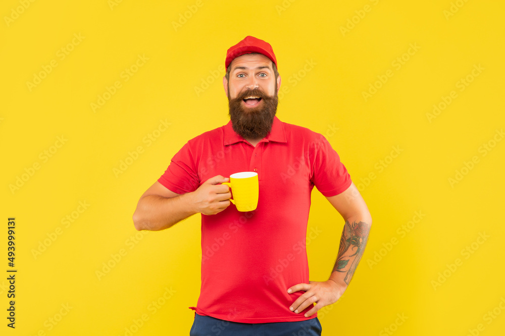 Surprised bearded man in casual red cap and tshirt holding mug yellow background, tea Surprised bearded man in casual red cap and tshirt holding mug yellow background, tea