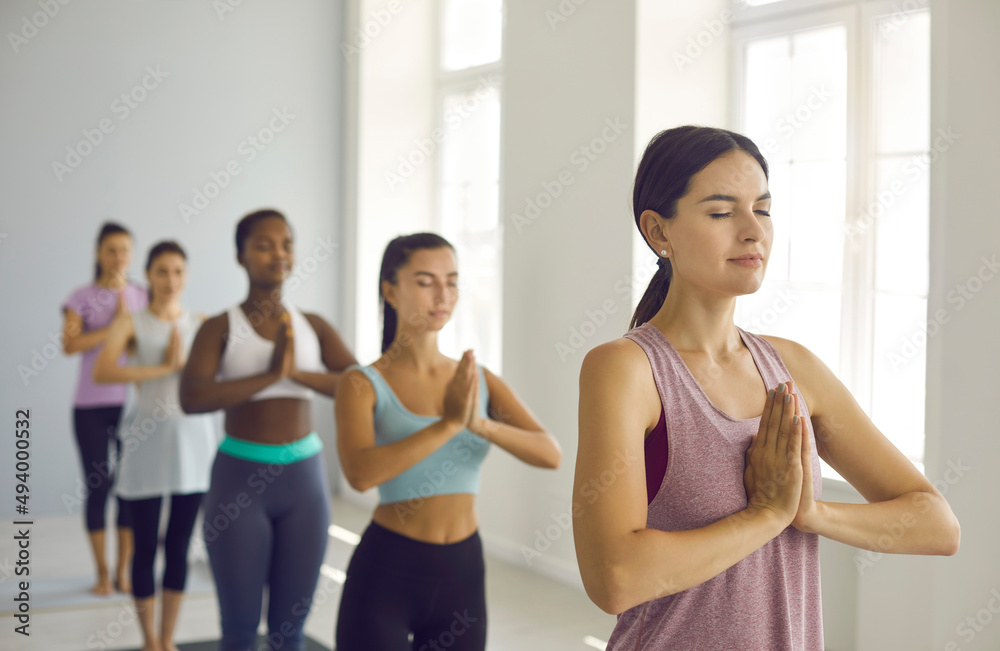 Diverse women in sportswear meditate together in modern sports fitness center or club relieve negative emotions. Multiracial young females practice yoga do workout training follow healthy lifestyle.