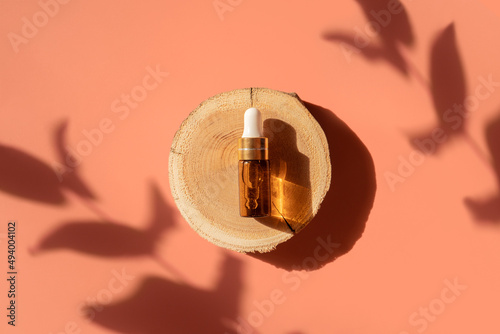 Amber glass dropper bottle on woodcut in the sunlight with eucalyptus flower shadows. Top view. Luxury and natural cosmetics presentation. Testers, beauty samples perfumery concept. Shades and lights © Lavsketch