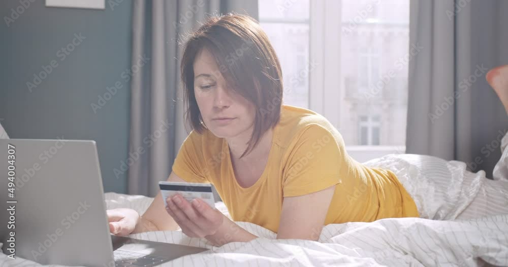 Young female working on notebook, typing on computer keyboard in bedroom and smiling. Happy caucasian woman lying on the bed and using laptop doing online shopping. Young female working on notebook, typing on computer keyboard in bedroom and smiling. Happy caucasian woman lying on the bed and using laptop doing online shopping.