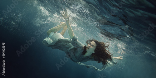 A woman in a dress swims under water as she flies in weightlessness