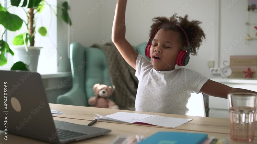 African child having study break and sitting at table with laptop in home interior spbd. Closeup view of cute little girl rests and looks at computer screen, listens to lecture with headphones and African child having study break and sitting at table with laptop in home interior spbd. Closeup view of cute little girl rests and looks at computer screen, listens to lecture with headphones and