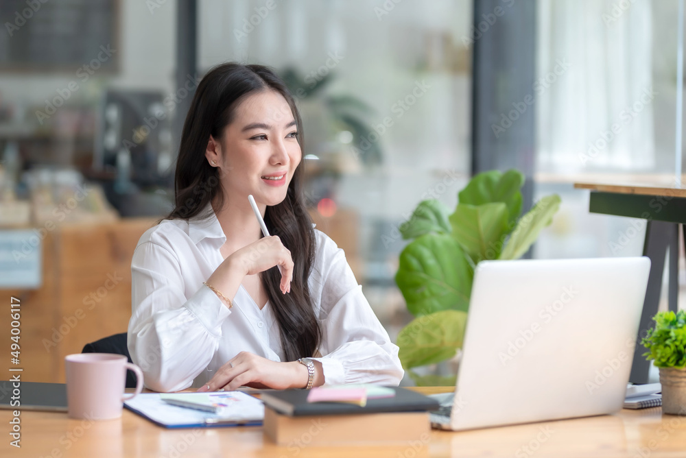 Fototapeta premium Pretty young Asian businesswoman sitting in office using laptop computer.