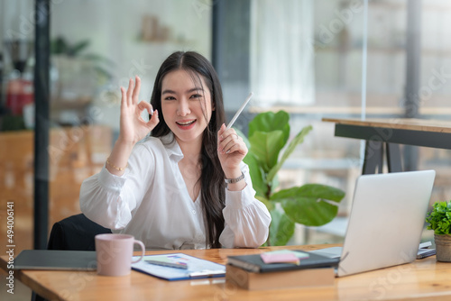 Pretty young Asian businesswoman sitting in office using laptop computer.
