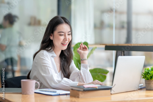 Pretty young Asian businesswoman sitting in office using laptop computer.