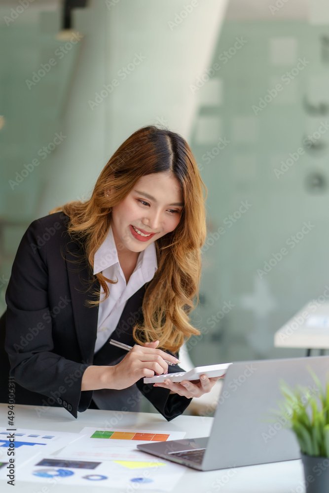 Young Asian businesswoman using a calculator to calculate business principles. Accounting statistics concept at the office. Young Asian businesswoman using a calculator to calculate business principles. Accounting statistics concept at the office.
