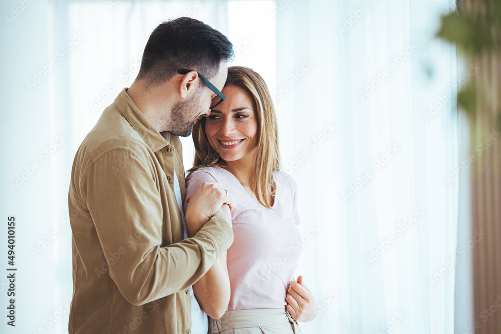 Young Couple Relaxing In Loft Apartment Looking Out Of Window. Couple drinking coffee and looking through the window. Happy girlfriend and smiling boyfriend looking away Young Couple Relaxing In Loft Apartment Looking Out Of Window. Couple drinking coffee and looking through the window. Happy girlfriend and smiling boyfriend looking away