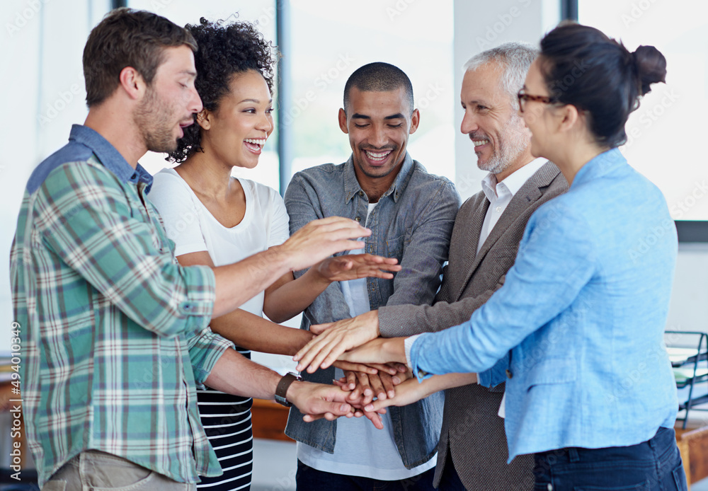 Obraz premium Pulling together. Shot of a group of happy coworkers standing with their hands together in huddle in an office.