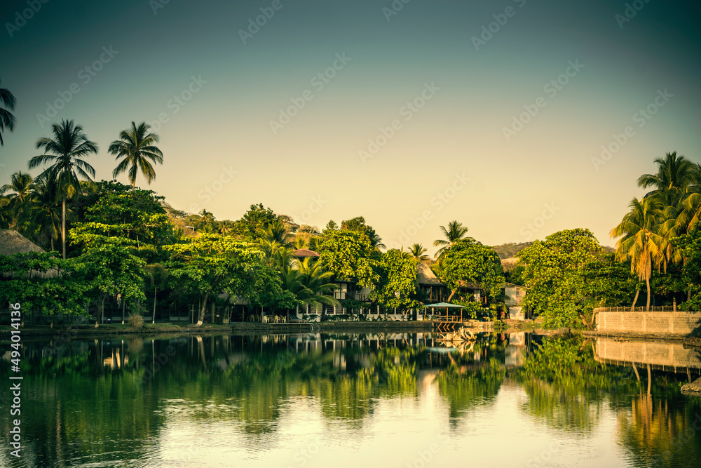 Obraz premium Sunset over touristic village in El Tunco, El Salvador. Huts covered by palm trees on the shore of Rio Grande river
