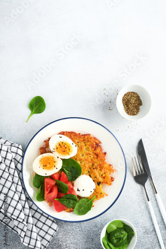 Breakfast. Potatoes latkes with sour cream, spinach salad, tomatoes and boiled eggs on light background. Delicious food for breakfast. Top view.