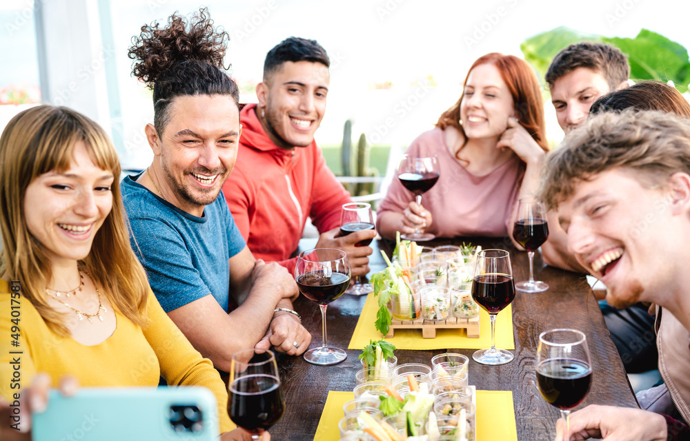 Trendy friends taking selfie at winery bar garden - Young people having fun together drinking red wine on restaurant reopening - Selective focus on left guy with night vivid filter and shallow depth