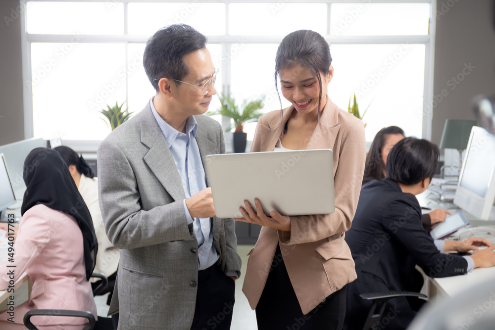 Asian businessman and businesswoman talking and looking laptop computer in the office, man standing explaining about financial with woman together, entrepreneur and employee planning about business. Asian businessman and businesswoman talking and looking laptop computer in the office, man standing explaining about financial with woman together, entrepreneur and employee planning about business.