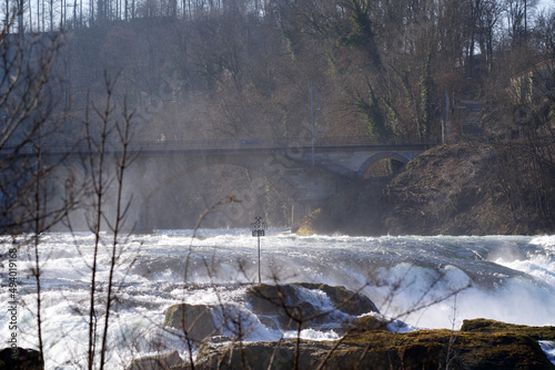 Famous Rhine Falls with rocks, spray and splashing water on a sunny spring day. Photo taken March 5th, 2022, Zurich, Switzerland.