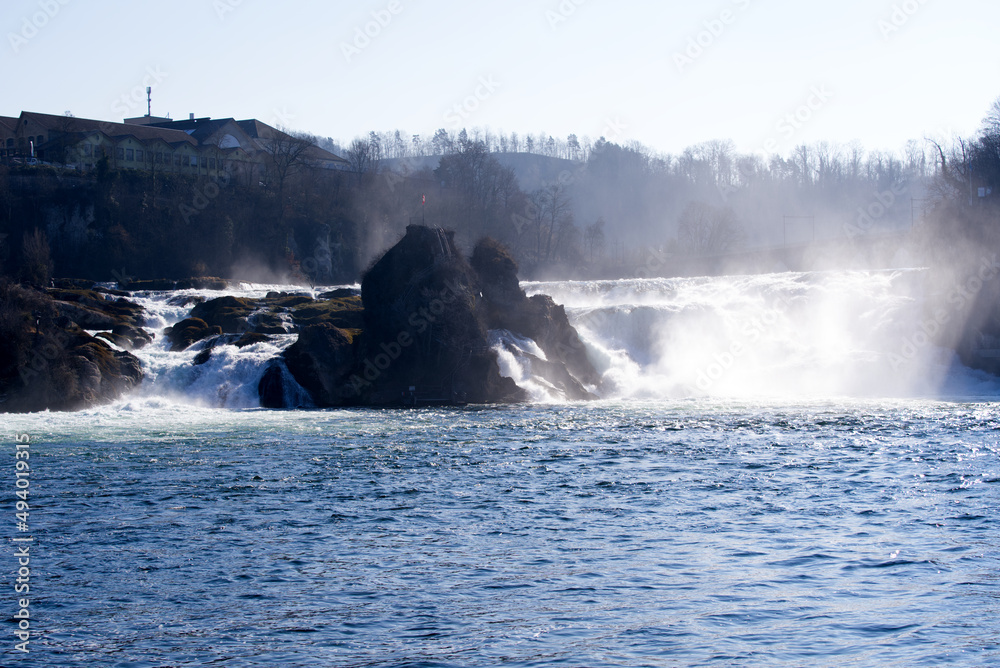 Famous Rhine Falls with rocks, Swiss flag and splashing water on a sunny spring day, focus on background. Photo taken March 5th, 2022, Zurich, Switzerland.