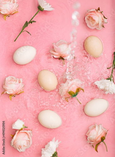Easter scene with rose flowers and eggs in water with bubbles. Minimal natural pastel pink background.