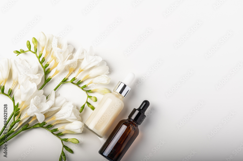 Bouquet of white freesias and two cosmetic serum with a pipette in a glass bottles on a white background. Bouquet of white freesias and two cosmetic serum with a pipette in a glass bottles on a white background.