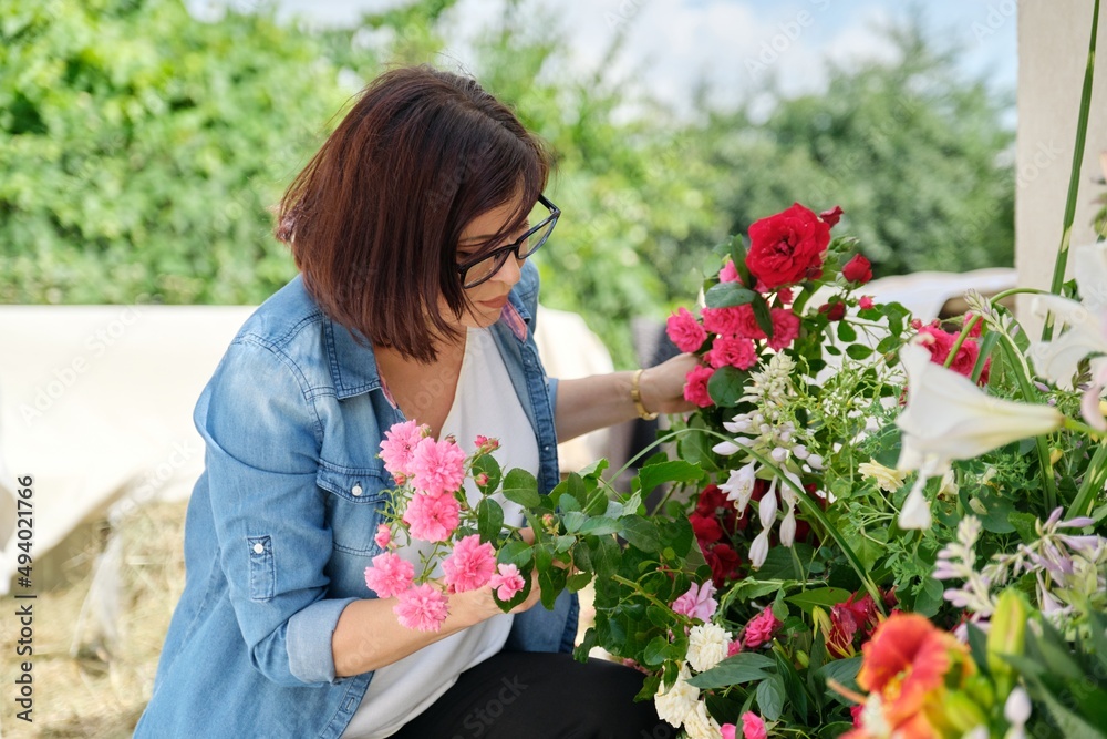 Fototapeta premium Woman florist making flower arrangement in basket outdoor.