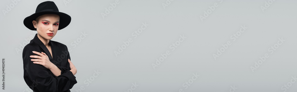 stylish woman in black blazer and brim hat looking at camera isolated on grey, banner. stylish woman in black blazer and brim hat looking at camera isolated on grey, banner.