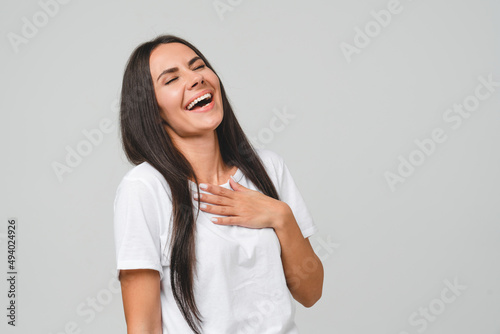 Smiling happy cheerful positive caucasian young girl woman laughing feeling amused wearing white T-shirt in good mood isolated in grey background