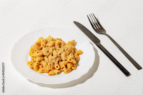 Curly Italian pasta with sauce on a white plate. Minimalism. White background. Pasta in cheese sauce. Knife and fork are black.