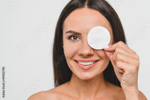 Closeup cropped portrait of caucasian young pretty woman lady girl female holding cotton pad for removing makeup cosmetics, applying daily creme cream mask on face skin for hydration isolated in white