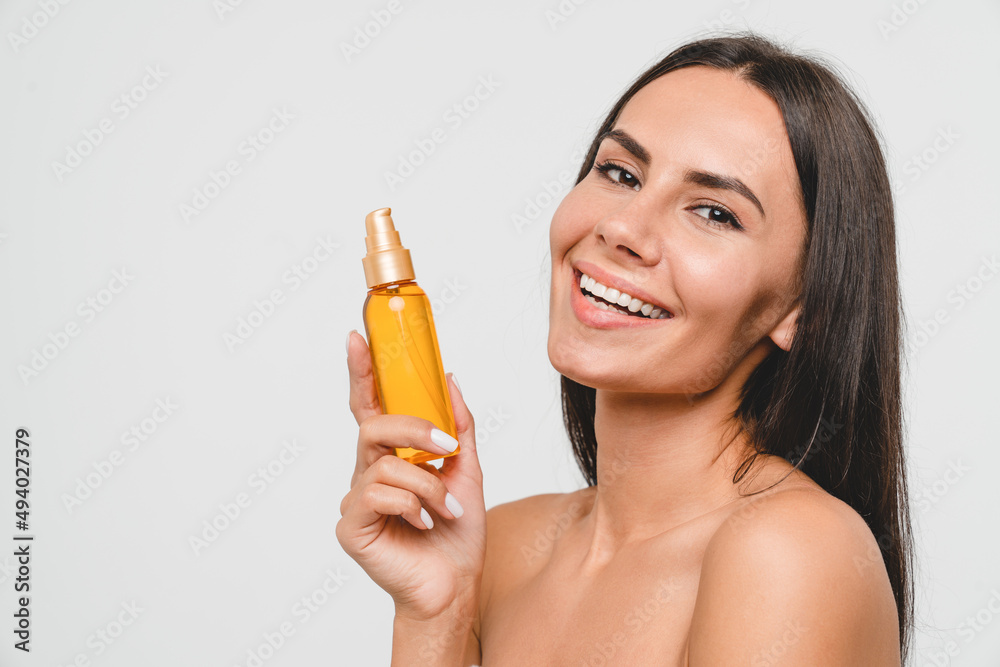 Smiling beautiful caucasian young woman lady female applying beauty care oil for soft skin face care, anti-wrinkle hydration dermatology beauty treatment isolated in grey background Smiling beautiful caucasian young woman lady female applying beauty care oil for soft skin face care, anti-wrinkle hydration dermatology beauty treatment isolated in grey background
