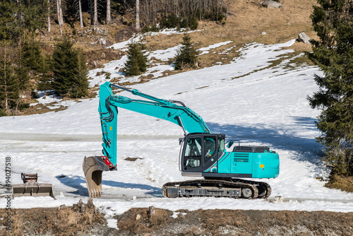 turquoise excavator in snowy landscape constructing a torrent control in the mountains photo