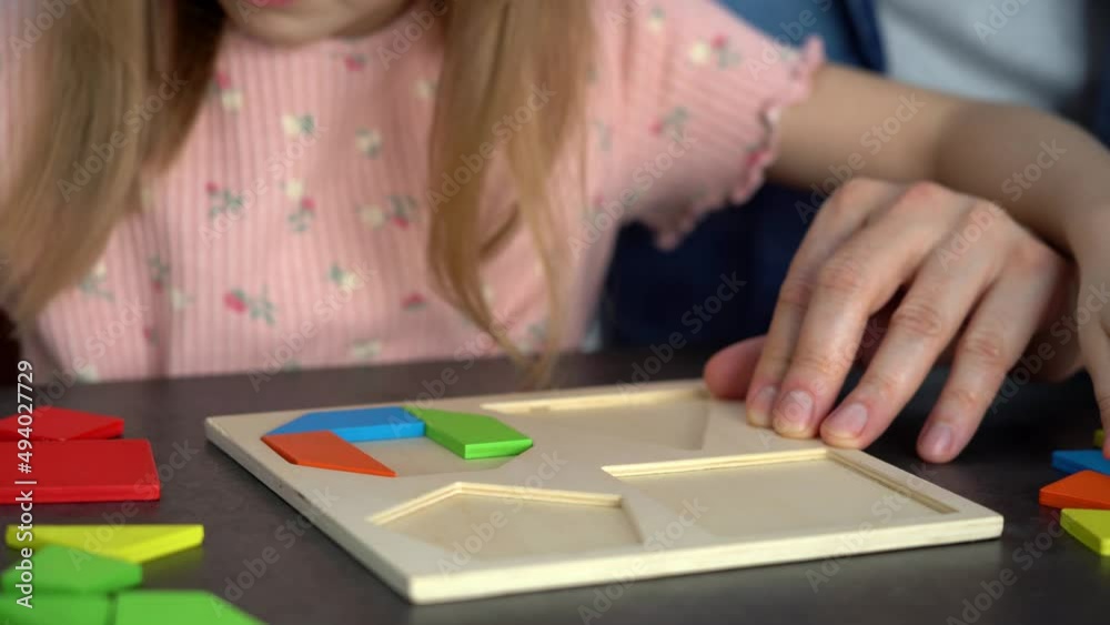 Close up of childrens hands put colored tangram puzzle. Family spends leisure time collect wooden jigsaw. Education Close up of childrens hands put colored tangram puzzle. Family spends leisure time collect wooden jigsaw. Education