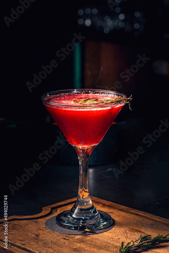 Martini red cocktail served on a tall martini glass served with a smokey garnish on a wood table