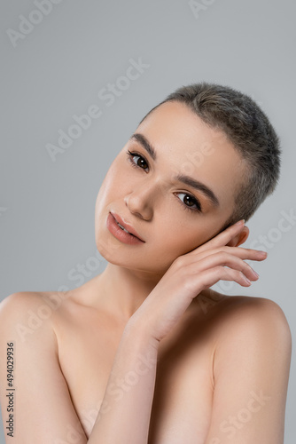 charming woman with natural makeup holding hand near face isolated on grey.