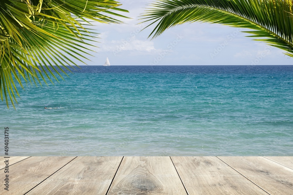 Wooden plank and palm leaves with clear blue water in the background