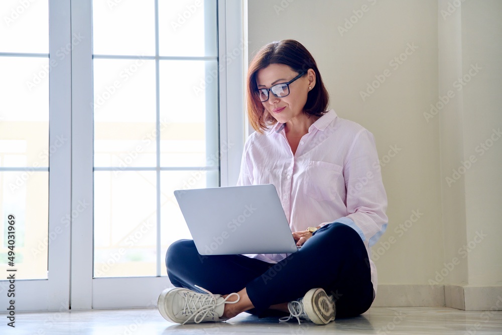Middle aged woman sitting on floor using laptop Middle aged woman sitting on floor using laptop