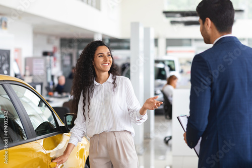 Middle eastern lady choosing new car, having conversation with sales manager