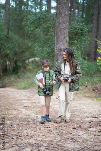 Boy and wo with cameras walking in forest. Dark-haired mother and son in coats getting ready to take pictures. Parenting, family, leisure concept