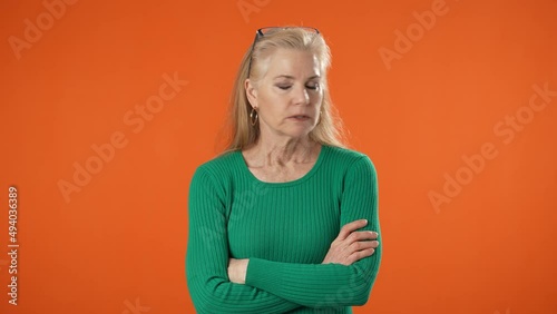 Portrait of frustrated angry irritated mature blonde woman 40s 50s years old in green casual shirt isolated on solid orange color background copy space studio photo