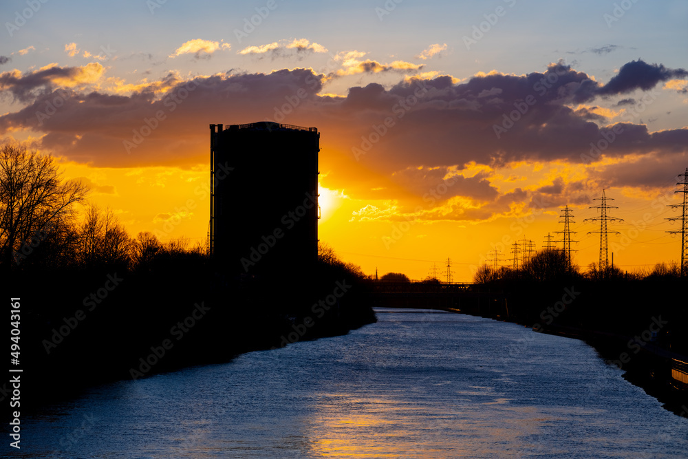 Inland ship canal “Rhein-Herne-Kanal“ at sunset in Oberhausen Ruhr Basin Germany. Skyline with historic Gasometer silhouette industriral monument on a sunny winters day with colorful sky gradient. 