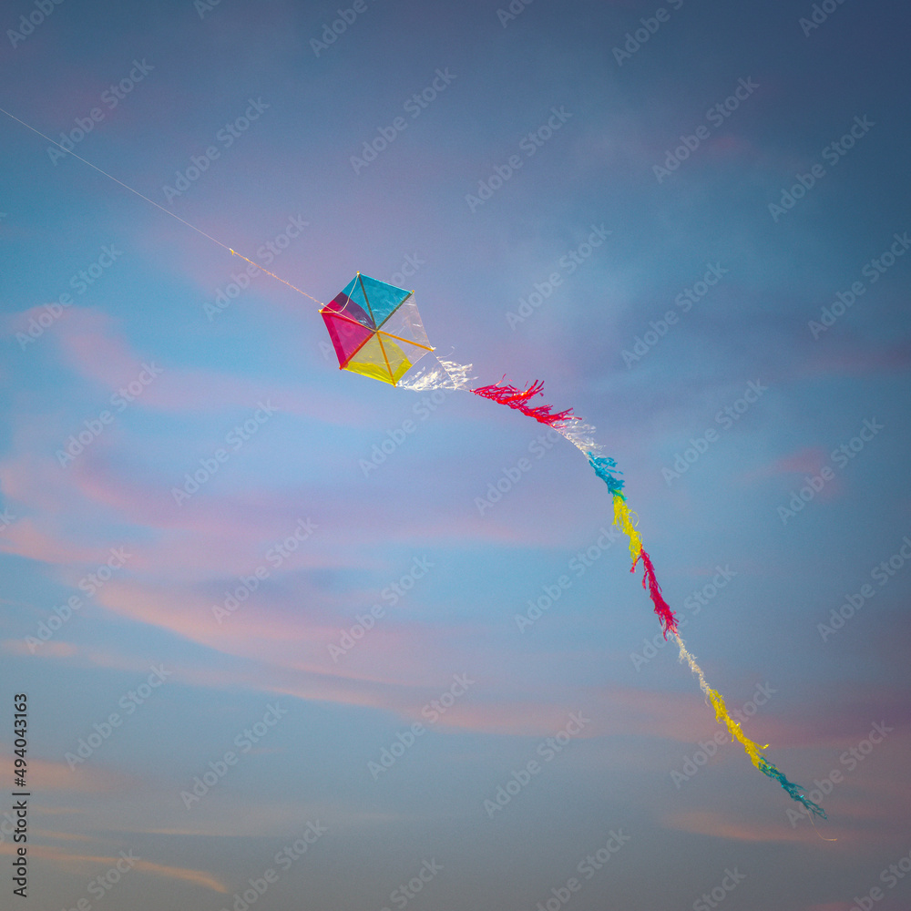 Colorful flying kite against a beautiful sunset - obrazy, fototapety, plakaty 