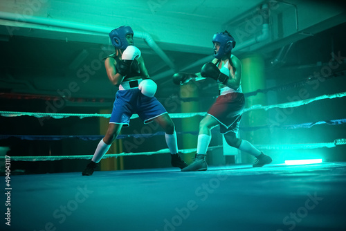 Strong boxer girls training sparring before competition. Two young girls in helmets and gloves actively boxing, demonstrating punches and skills to trainer. Healthy lifestyle and extreme sport concept