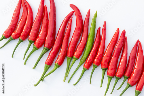 Chili pepper, red and one green, in row on white paper. Stand out concept. Similarity versus difference. Copy space for text