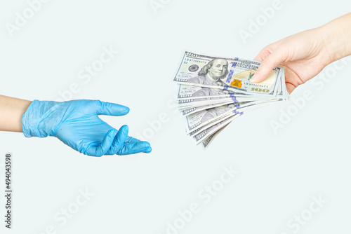 Treatment payment concept. Transfer of money from hand to another hand in blue medical glove. Bribe to the doctor. Paid medicine concept.