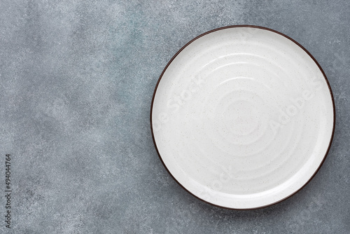 Empty white plate on gray concrete background. Top view, flat lay.