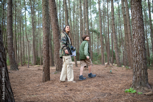 Content boy and woman with cameras walking in forest. Dark-haired mother and son in coats looking around. Parenting, family, leisure concept © KAMPUS
