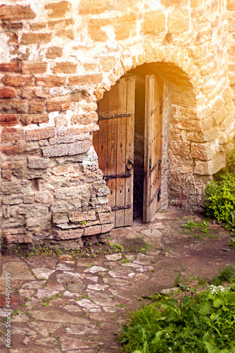 The road to the ajar wooden door in the stone wall of the ancient fortress in the rays of the sun.
Ivangorod fortress, Russia