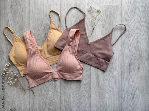 Three different bra tops, top view. Basic crotops in beige, pink and coffee on wooden background. Lingerie photo