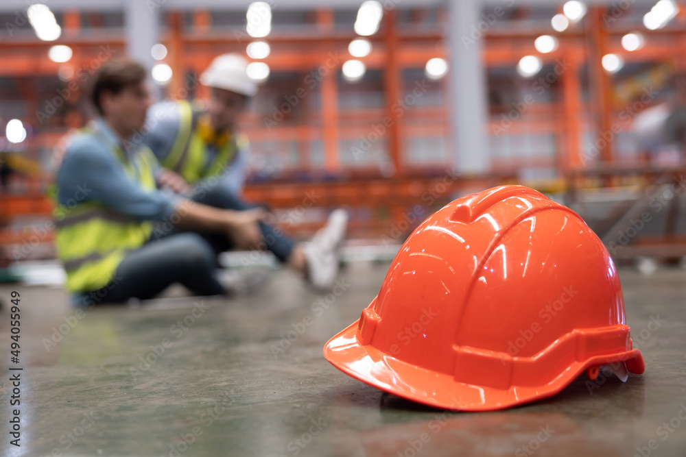 Red Hard Hat with Blurred Injured Factory Workers as Background Red Hard Hat with Blurred Injured Factory Workers as Background